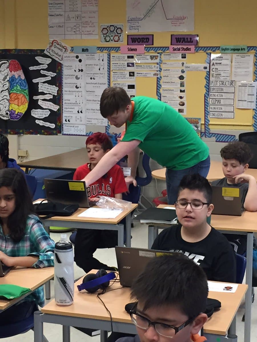 A teacher helping students code on their laptops